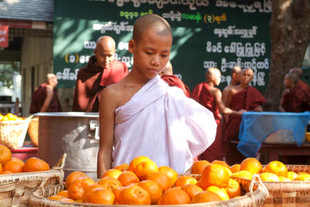 Mandalay, Myanmar, 17 January 2010: Young monk in the kitchen in front of a pile of oranges at Mahagandayon Monastery on Mandalay, Myanmarのeditorial素材