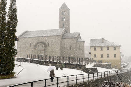 woman walking under snowfall in front of Saint Nicolao church at Giornico on Leventina valley on the Swiss alpsの写真素材