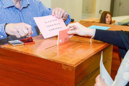 Lugano, Switzerland - 11 april 2016: Hand putting a voting ballot in a slot of wooden box at the...