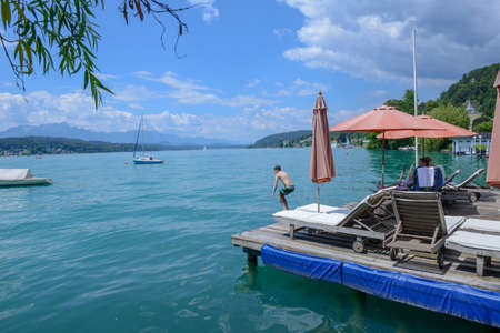Portschach, Austria - 1 July 2018: Sunchairs on wooden pier and view of beautiful alpine lake Worthersee on Austriaのeditorial素材