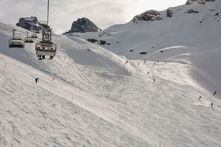 Engelberg, Switzerland - 3 March 2019: People skiing and going up the mountain by chairlift at...