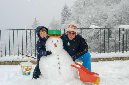 Happy boy and father playing with a snowman in the gardenのeditorial素材