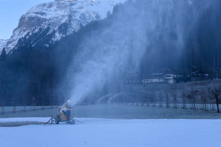 Snow-machine bursting artificial snow over a skiing slope at Engelberg on the Swiss alpsの写真素材