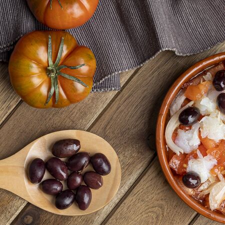 Esqueixada in clay pot and wooden spoon with some black olives on black napkin. zenith viewの写真素材