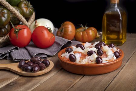 Cod with tomato in clay casserole with Organic food vegetables in wicker basket on rustic wooden table.の写真素材