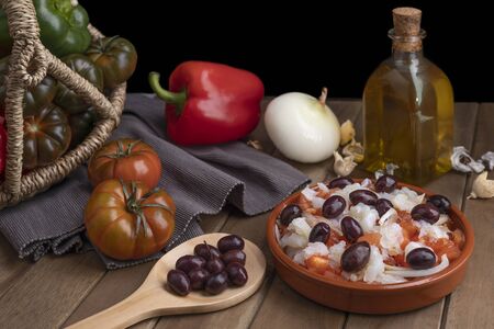 Esquexada in clay pot with ingredients and wooden spoon with some black olives.の写真素材