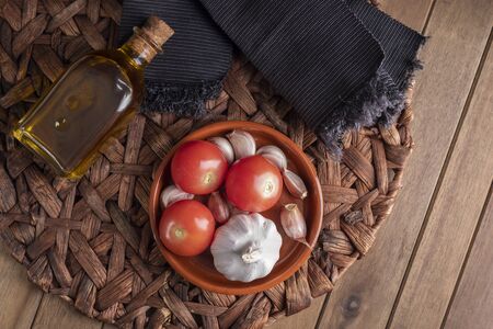 Clay pot with garlic and tomatoes next bottle of extra virgin oil and black napkin. zenith view.の写真素材