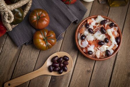 Esqueixada in clay pot and wooden spoon with some black olives on black napkin. zenith view.の写真素材