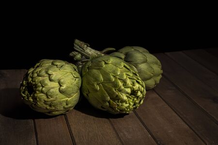 Artichokes on wooden table with black background.の写真素材