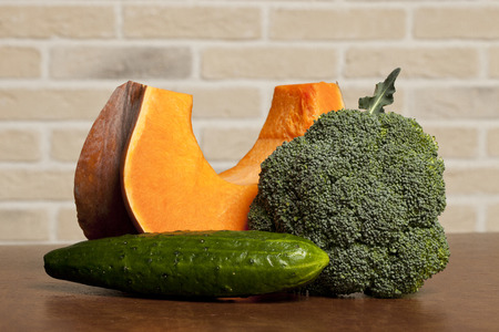 Pumpkin, cucumber and cauliflower on brown table on brickwork backgroundの写真素材