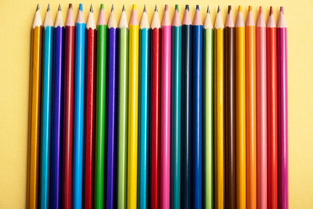 There are many different colored pencils lying exactly in a row on a colored background.