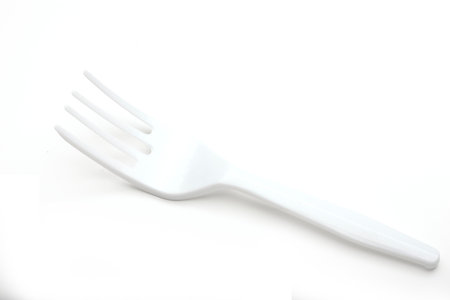 A single white plastic fork lies on a plain white background. The fork has three prongs and a smooth handle, suitable for casual dining or picnics.の写真素材