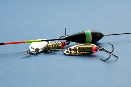 Fishing tackle including a float and lures on a blue background. The float is black with green and...
