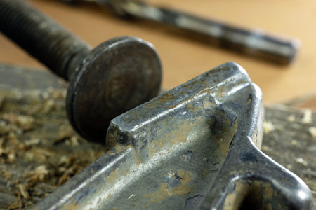 Close-up of a metal clamp and screw on a wooden surface. The clamp is used for holding materials...