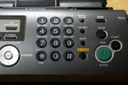 A close-up of a retro telephone with an answering machine. The device features a numeric keypad, buttons for functions like fax and copy, and a green start button.の写真素材