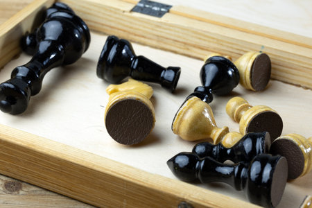A collection of black and white chess pieces scattered in a wooden box.