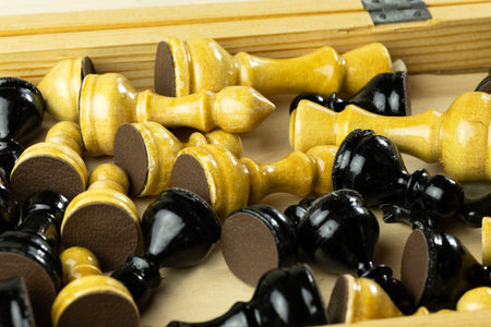 A collection of wooden chess pieces in black and white colors scattered inside a wooden box.