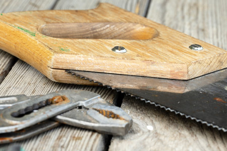 Close-up of a wooden-handled hand saw resting on a wooden surface.