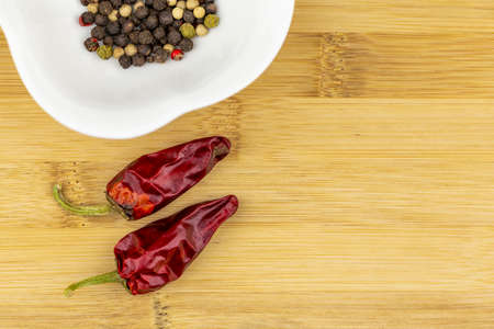 Two chilli peppers and a selection of pepper seeds on white bowl on a chopping boardの写真素材