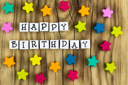 The text happy birthday arranged from blocks on a wooden background, next to colorful stars