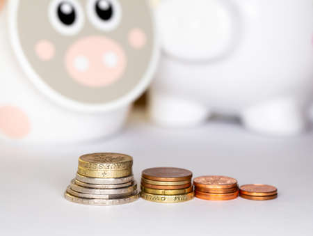 White porcelain piggy bank and a large amount of small coins. Object illuminated by artificial...