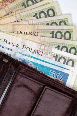 Lots of Polish banknotes sticking out of a brown leather wallet. Photo taken under artificial, soft...