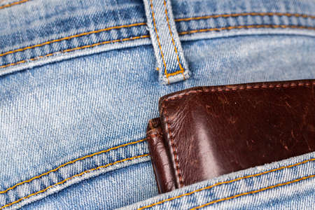 Leather wallet sticking out of the back pocket of denim pants. Photo taken under artificial, soft lightの写真素材