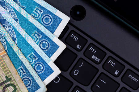 A set of Polish PLN 50 and 100 banknotes arranged on a black laptop keyboard. Photo taken under...