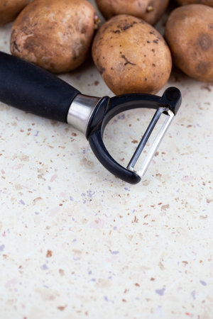 Several organic potatoes and a potato peeler on the table. Made in natural light, soft shadows.の写真素材