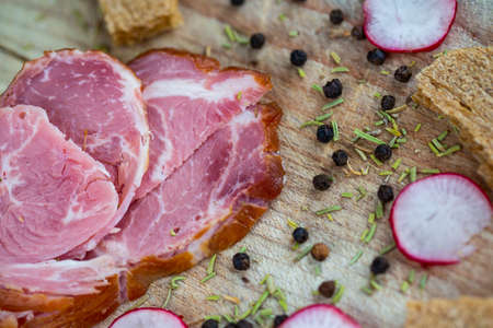 Slices of ham, radishes, crisp bread and peppercorns on a wooden chopping board