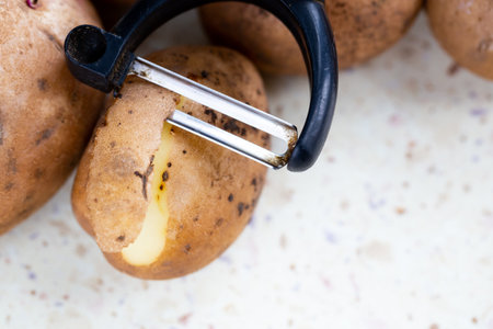 Several organic potatoes and a potato peeler on the table. Made in natural light, soft shadows.の写真素材