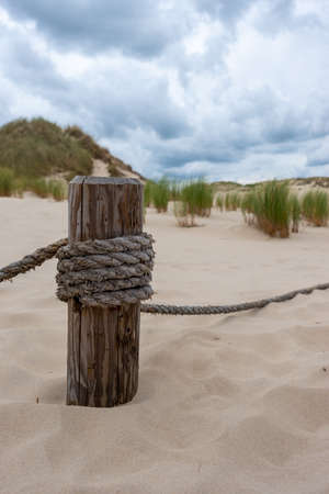 A wooden post with stretched ropes separating the hiking trail from the protected area. Photo taken in good lighting conditions on a cloudy dayの写真素材