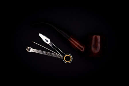 A pipe for smoking tobacco and accessories for its cleaning on a black background.の写真素材