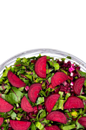 Fresh, cut leaves and beetroot pieces arranged in a glass bowl. Photo taken under artificial, soft...