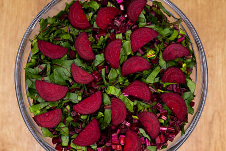Fresh, cut leaves and beetroot pieces arranged in a glass bowl. Photo taken under artificial, soft light.の写真素材