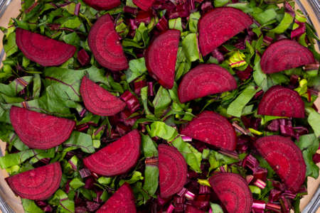 Fresh, cut leaves and beetroot pieces arranged in a glass bowl. Photo taken under artificial, soft...