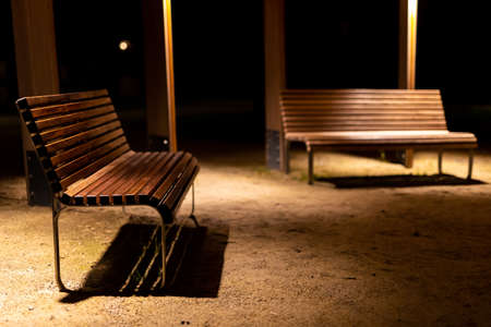 A park shed with empty benches during a pandemic. Meeting places without people. The photo was taken at night with artificial street lighting.の写真素材