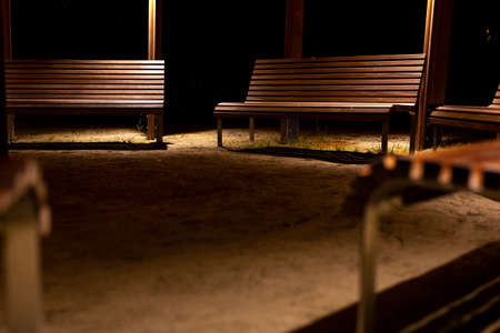 A park shed with empty benches during a pandemic. Meeting places without people. The photo was taken at night with artificial street lighting.の写真素材