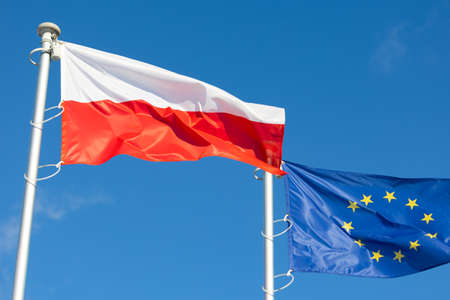 The flags of Poland and the European Union waving against the blue skyの写真素材