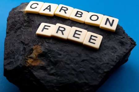 A lump of coal arranged on a blue background with the sentence "carbon free" composed of letters. Photo taken under artificial, soft lightの写真素材