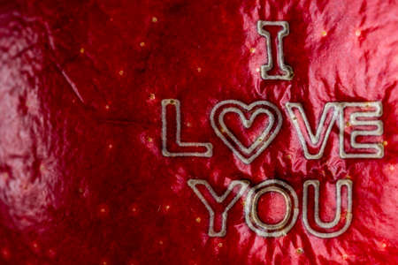 The wording "I Love You" laser engraved on the skin of a red apple. Scene lit by uniform, soft light.の写真素材