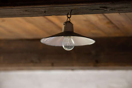 Old electric lamp on the ceiling of an abandoned wooden house. Photo taken in low light conditions.