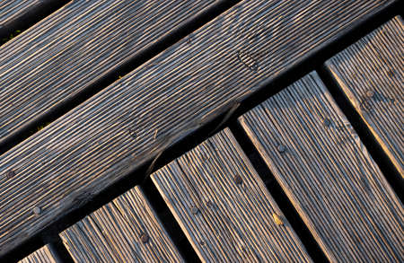 A play of lights and shadows on the boards of a wooden pier. The light falling on the boards at a...