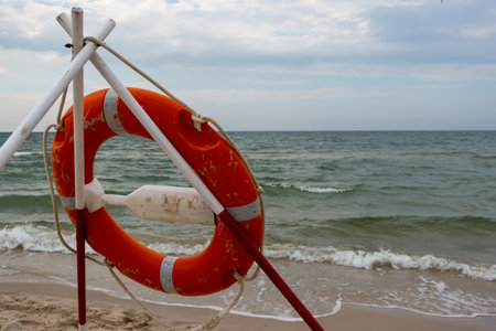 An orange lifeboat and reach extenders stuck in the sand on the beach. In the background, a view of...