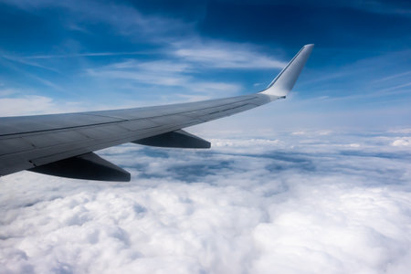 View from the plane window to the wing. Photo taken while flying above the clouds. In the distance,...