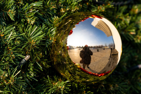 Reflection of a photographer taking a photo in a Christmas ball hanged on a city Christmas tree. Christmas tree made of artificial materials.の写真素材