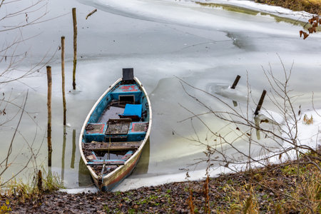 An old fishing boat in an abandoned fishing harbor on an ice-bound river. Photo taken in winter, sheets of ice near the shore.の写真素材