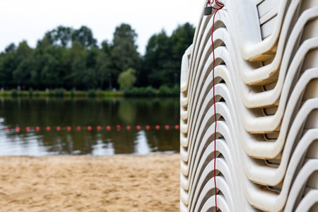 Beach loungers stacked after the summer season on the city beach by the pond. The end of recreational activity at the beginning of autumnの写真素材