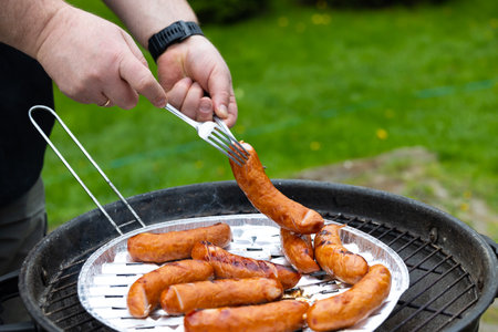 The hands of a person holding two forks change the position of the sausage on the grid of the garden grill. Photo taken in natural lighting conditions.の写真素材