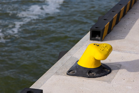 Yellow mooring hook on the concrete quay. Safety of boats moored to the waterfront. Photo taken on a sunny dayの写真素材